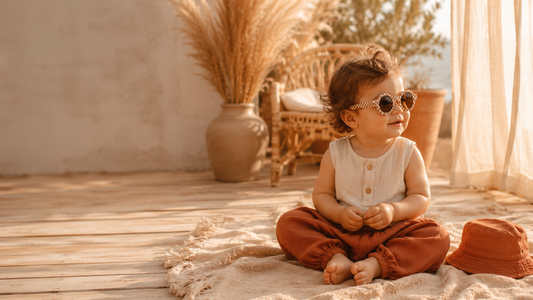 Bébé en look d'été bohème avec lunettes de soleil rondes à damier sur une terrasse en bois, ambiance dorée