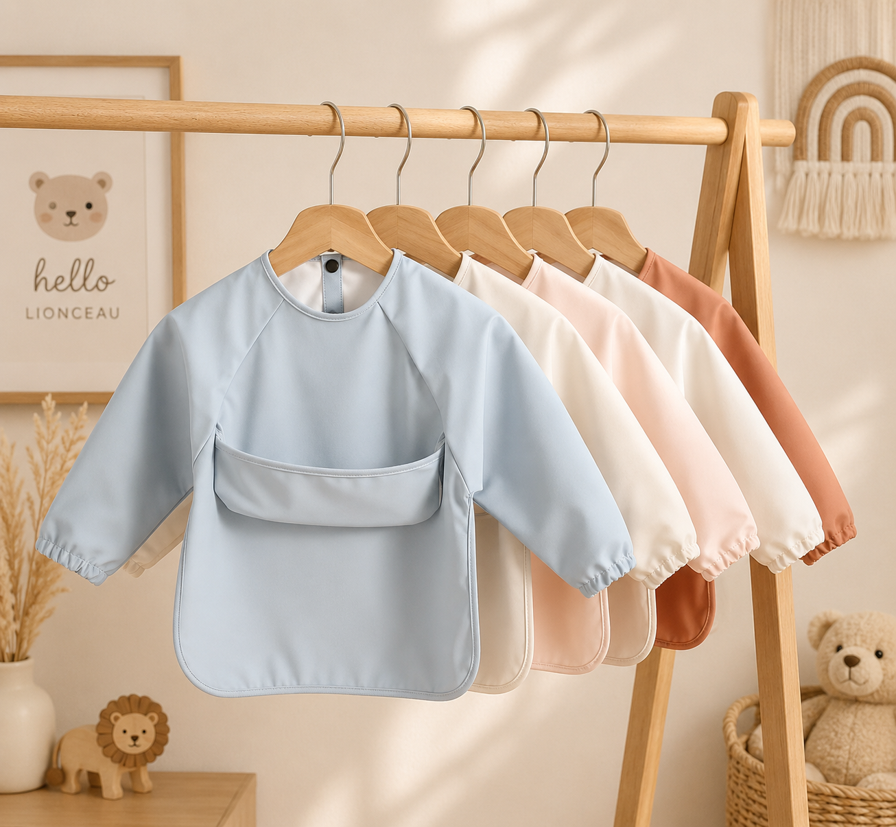 Lot de tabliers de peinture imperméables pour bébé et enfant suspendus sur un portant en bois dans une chambre bohème aux tons doux et naturels.