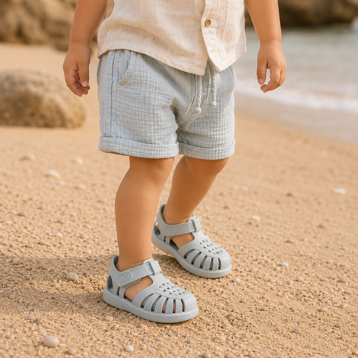 Sandales gladiateur bébé bleu pastel portées par un petit garçon sur une plage au style bohème naturel.